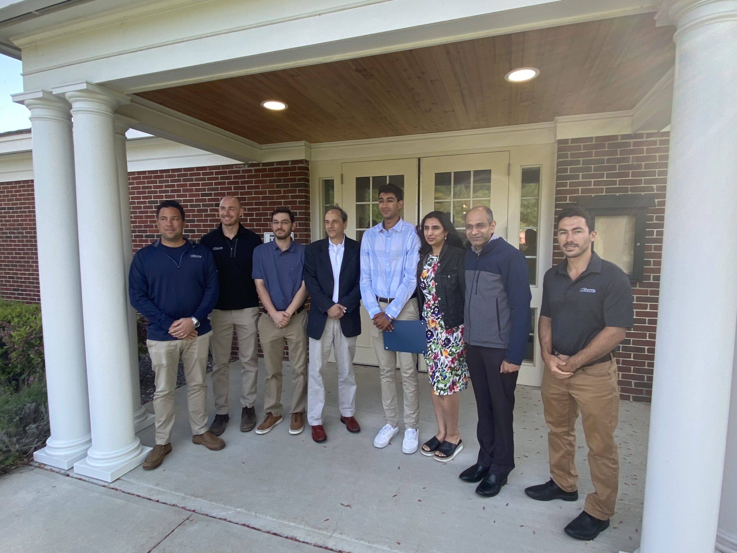 Group of people standing on a covered brick porch outside a school building.