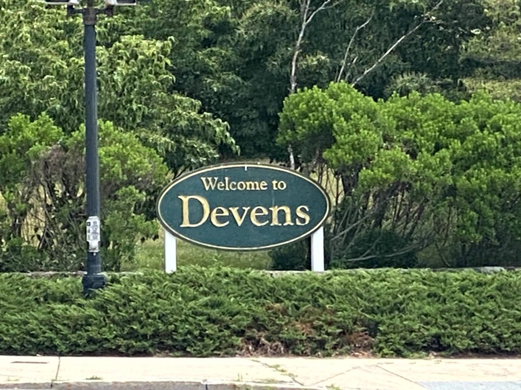 Welcome to Devens sign set in a landscaped area with shrubs and trees.